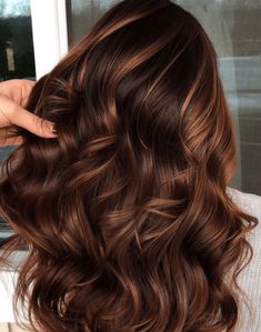 a woman with long brown hair is holding her hand over her head and looking out the window