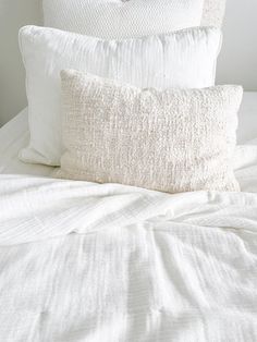 a bed with white linens and two pillows on top of each other in front of a window