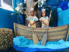 two children are standing in front of a fake wooden boat with oars on it