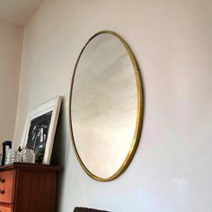 an oval mirror hanging on the wall above a dresser