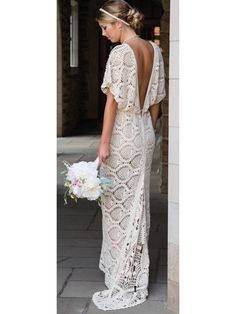 the back of a woman in a white lace dress holding a bouquet and looking down