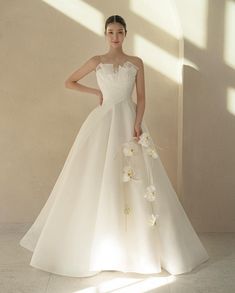 a woman in a white wedding dress with flowers on the skirt and her hand on her hip