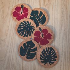 four coasters decorated with tropical leaves on a wooden surface, one is red and the other is blue