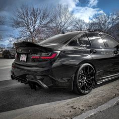 the rear end of a black car parked in front of a parking lot on a cloudy day