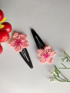 two crocheted hair clips sitting next to some cherry tomatoes and flowers on a white surface