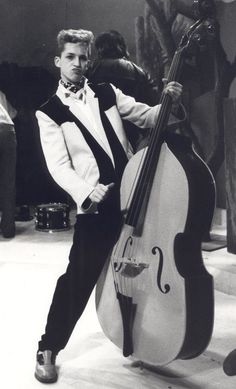 a man in a tuxedo poses with his cello on the set of an old movie