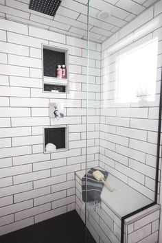 a white tiled bathroom with black flooring and shelves on the wall, along with a walk in shower