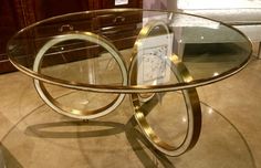 a glass and metal table on display in a living room with a couch behind it