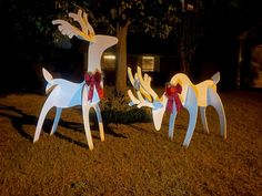 two paper reindeers are standing in the grass at night with red bows on their necks