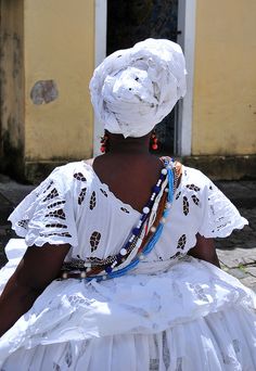 a woman in a white dress and headdress sitting on the ground with her back to the camera