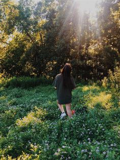 a woman walking through a lush green forest filled with wildflowers on a sunny day