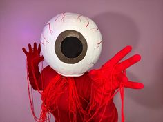 a person in a red costume with an eyeball on their head and hands up