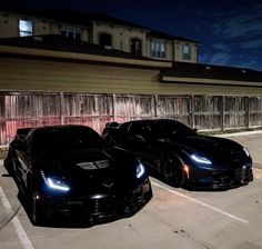 two black sports cars parked next to each other in a parking lot at night time