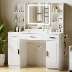 a white vanity with a mirror and lights on it next to a potted plant