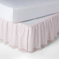 a white bed with a pink ruffled bedskirt on it's side