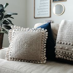 two crocheted pillows sitting on top of a couch next to a potted plant