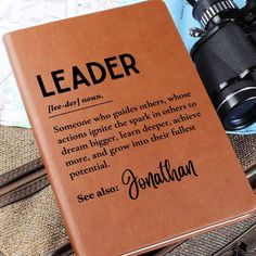 a leather book with the words leader written on it next to a pair of binoculars