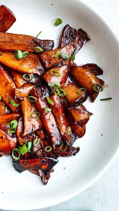 a white plate topped with cooked carrots and green onions