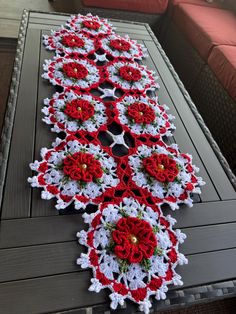 a crocheted table runner with red and white flowers sitting on top of it