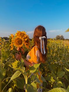 a woman standing in a sunflower field with her back to the camera and holding a flower