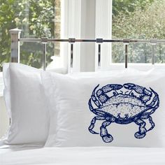 a white bed topped with two pillows and a blue crab pillow on top of it