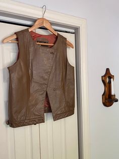 "Vintage brown leather vest Asymmetrical front closure One button missing and one button loose at the waist, pictured Chest: 34\" Length (shoulder to hem): 20\"" Fall Leather Sleeveless Jacket, Vintage Leather Vest Outerwear, Leather Vest Jacket For Fall, Brown Leather Vest For Workwear, Brown Leather Spring Vest, Brown Leather Vest For Spring, Brown Leather Sleeveless Vest, Brown Leather Vest, Women Waistcoat