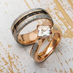 two gold rings with white and black diamonds in them on a wooden surface, one has a square cut diamond