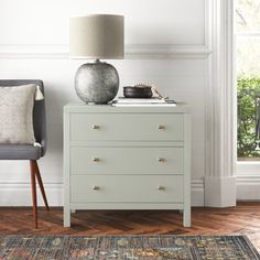 a white chest of drawers next to a gray chair with a lamp on the top