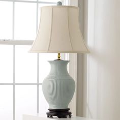 a light blue vase sitting on top of a white table next to a lamp shade