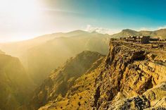 the sun shines brightly in the mountains above a city on top of a cliff