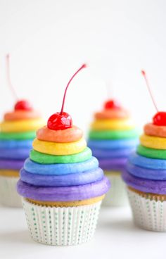 cupcakes with rainbow icing and cherries on top are sitting next to each other