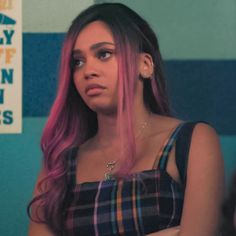 a woman with pink hair is standing in front of a blue and green wall, looking at the camera