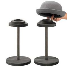 a person holding a hat on top of two metal stands with one hand and the other