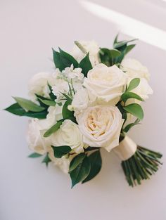 a bridal bouquet with white flowers and greenery on the top is laying on a table