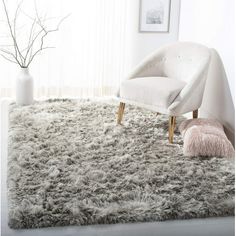 a white chair sitting on top of a shaggy rug next to a vase with flowers