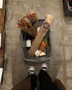 a person standing in front of a shopping cart with vegetables and groceries sitting on the floor