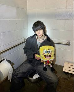 a man sitting on top of a toilet holding a spongebob pillow