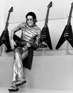 a man sitting on top of a wall with guitars behind him