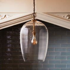 a glass light fixture hanging from a ceiling in front of a brick wall and fireplace