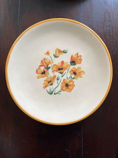 an orange and white bowl with flowers painted on the side sitting on a wooden table