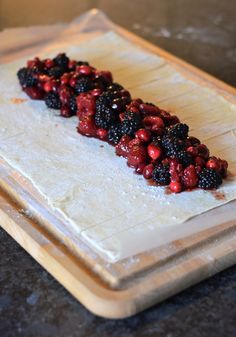 berries and raspberries are arranged on a piece of parchment paper that is sitting on a cutting board