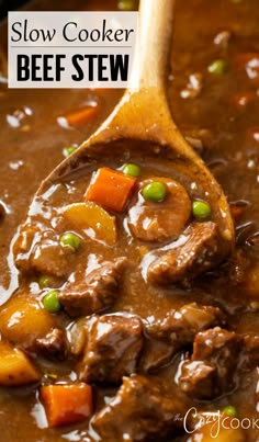 a wooden spoon filled with beef stew on top of a table