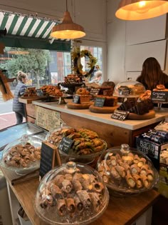 a woman is standing in front of a bakery counter filled with pastries and desserts