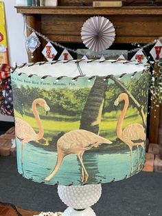 a lamp shade with flamingos on it sitting on top of a table in front of a fireplace