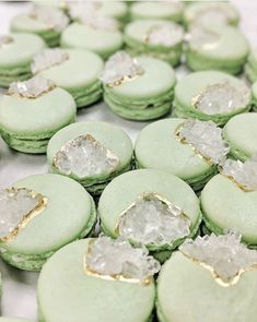 green macaroons with gold trim and white frosting on them are arranged in rows