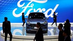 people walk past a car on display at an auto show