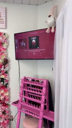 a tv mounted to the side of a wall next to a pink chair and tree