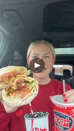 a woman holding up a taco and a drink in her hand while sitting in the back seat of a car