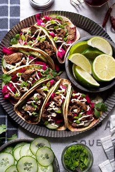 there are several tacos on the plate with cucumbers and limes around them