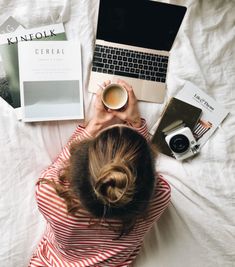 a woman laying on top of a bed next to a laptop computer and cup of coffee